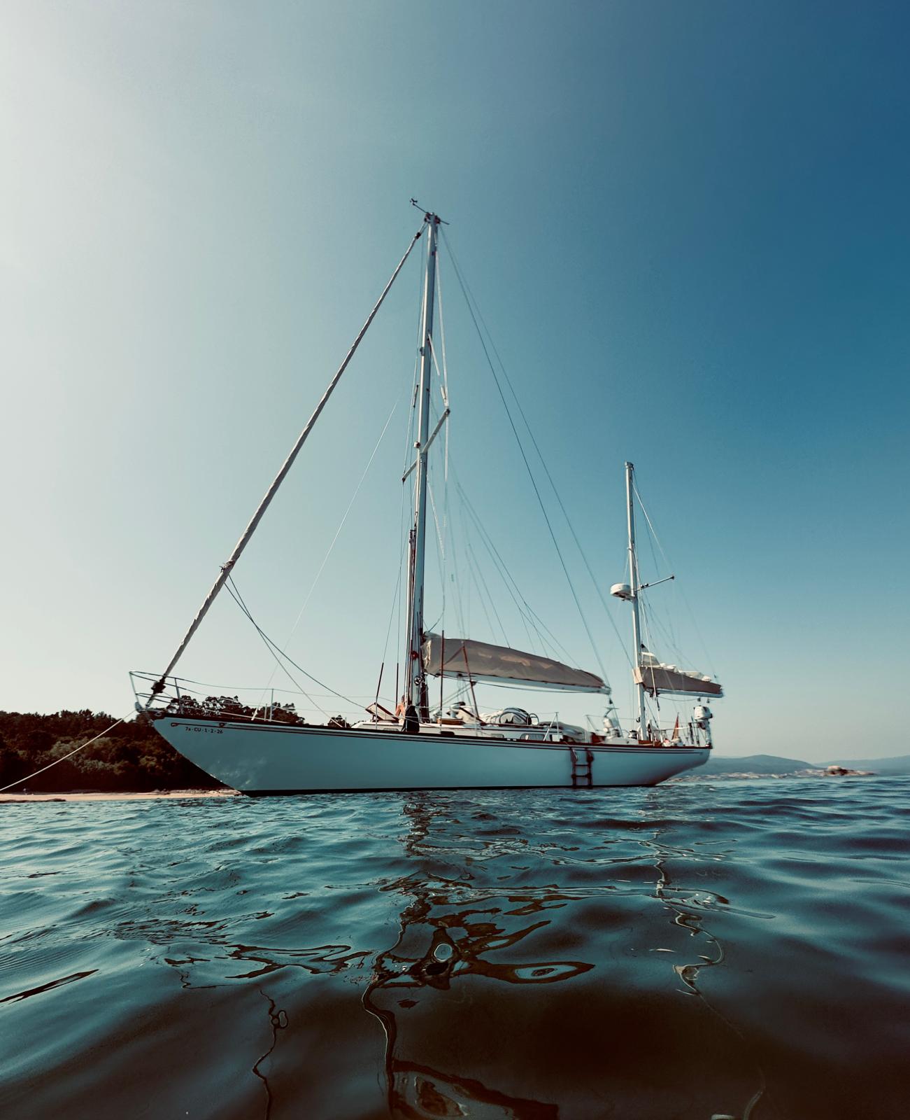 Malabar at anchor close to a sandy beach, awning rigged, low water-level view
